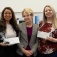 L to R: Jessica Flores, holding an envelope and gift, Allison Brashear, and Paige Guy holding an envelope and gift, all standing togehter and smiling. 