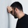 A man leans against a wall with his head on his arm, looking distraught. 
