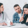 A doctor listens to the concerns of a young couple, the woman looks distressed and the man looks worried. 
