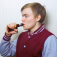 A teen boy wearing a letter jacket uses a vape. 