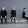 Three people sitting on a sculptural bench that looks like a tree branch. 
