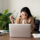 Woman sits at a laptop, holds eyeglasses with one hand and pinching her nose with the other. 